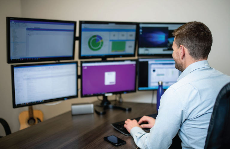 Staff member works on a 6-monitor computer workstation at desk