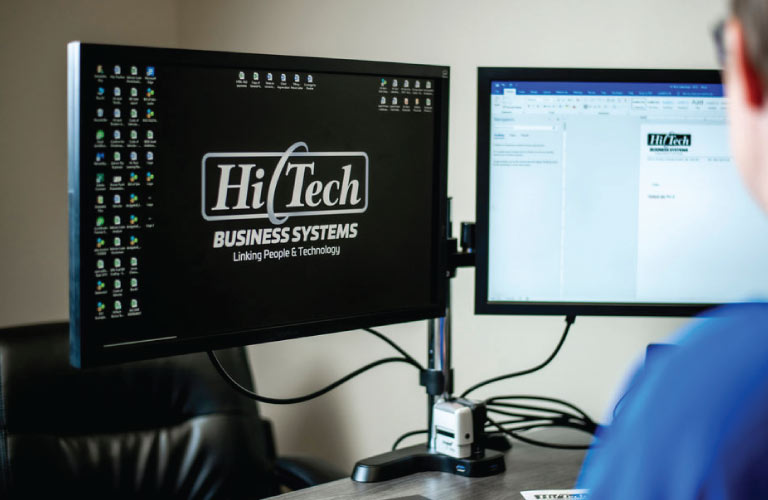 Hi-Tech employee edits a document on a dual-screen computer in his office in Grande Prairie