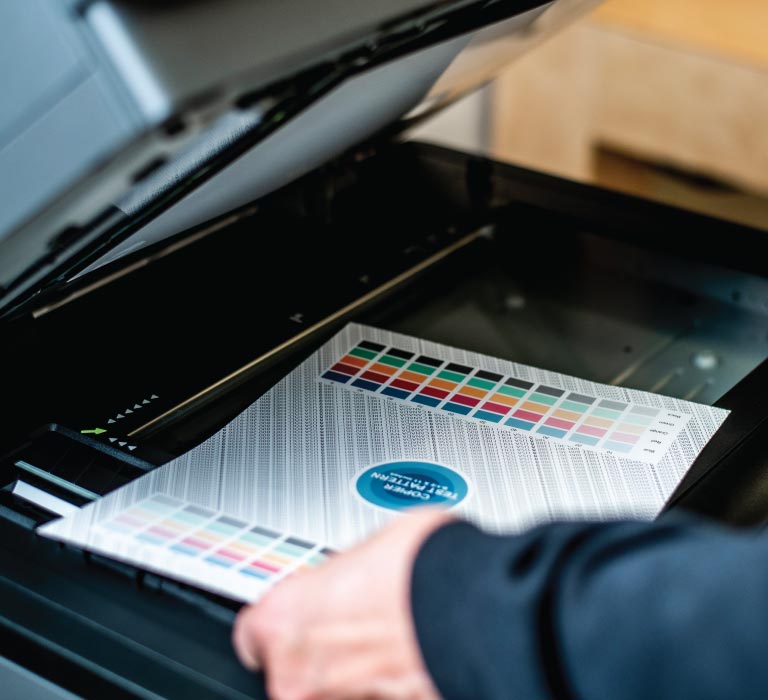 An employee tests a photocopier with a color and pattern test sheet to ensure its working properly