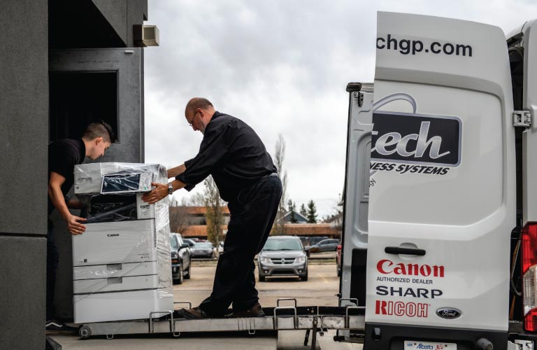 Two staff load a photocopier rental unit onto a delivery van for a office equipment rental customer