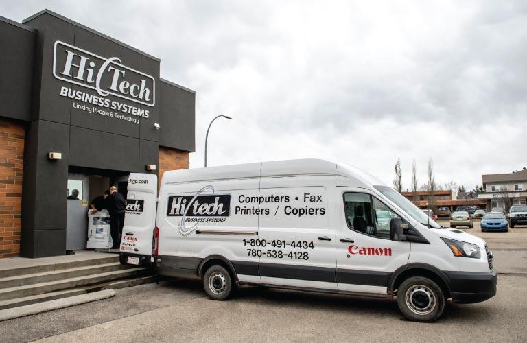 Technicians loading copier into delivery van from front door of Hi-Tech office