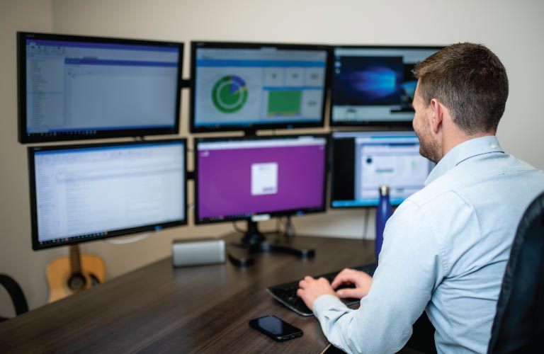 Employee works on computer with 6 monitors mounted to a 6 monitor stand